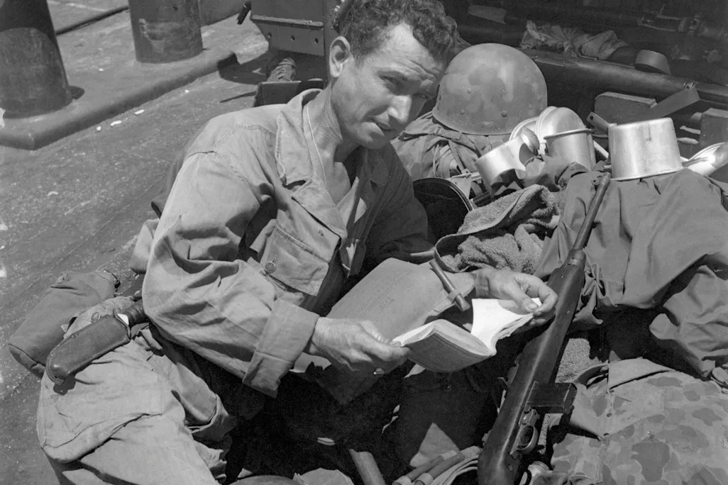 Bound for Morotai Island, Private Bryan Carroll, Memphis, TN, relaxes on the deck of an LST with a book. He leans on a pile of his belongings, which include his helmet and mess kit. 