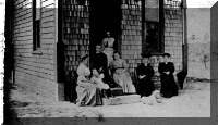 [A meeting of the Library Association at the first library building. From left, they are Mrs. Mary E. Akins, Catherine McMinn (child), Mrs. Ida Wheeler, Mrs. Levi Packard, Sr. (standing), Mrs. Mabel L. Saunders (who donated the building), Mrs. Julia Davidson, and Mrs. Fanny M. Grant.]